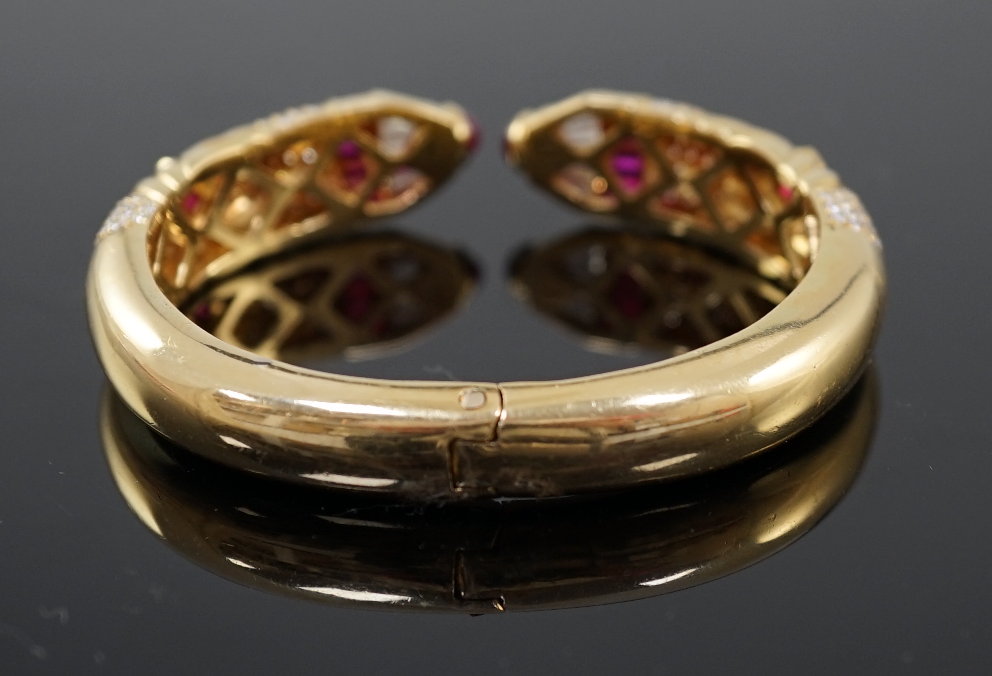 A modern 18ct gold, ruby and diamond cluster openwork hinged bangle